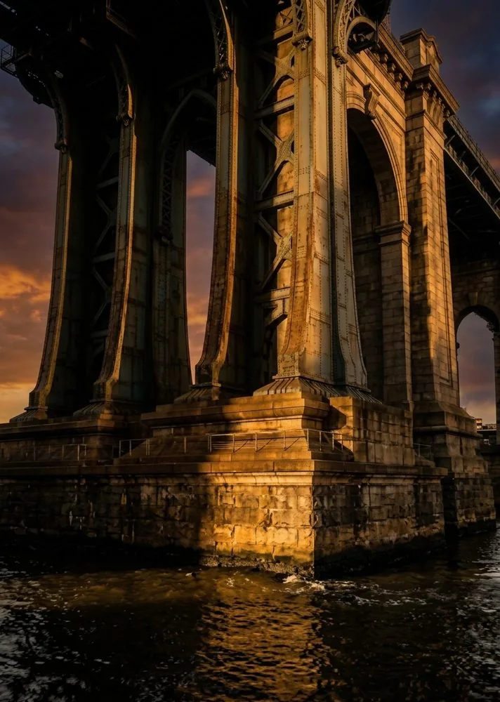 Vista de baixo dos pilares de pedra de uma ponte antiga, iluminados ao entardecer